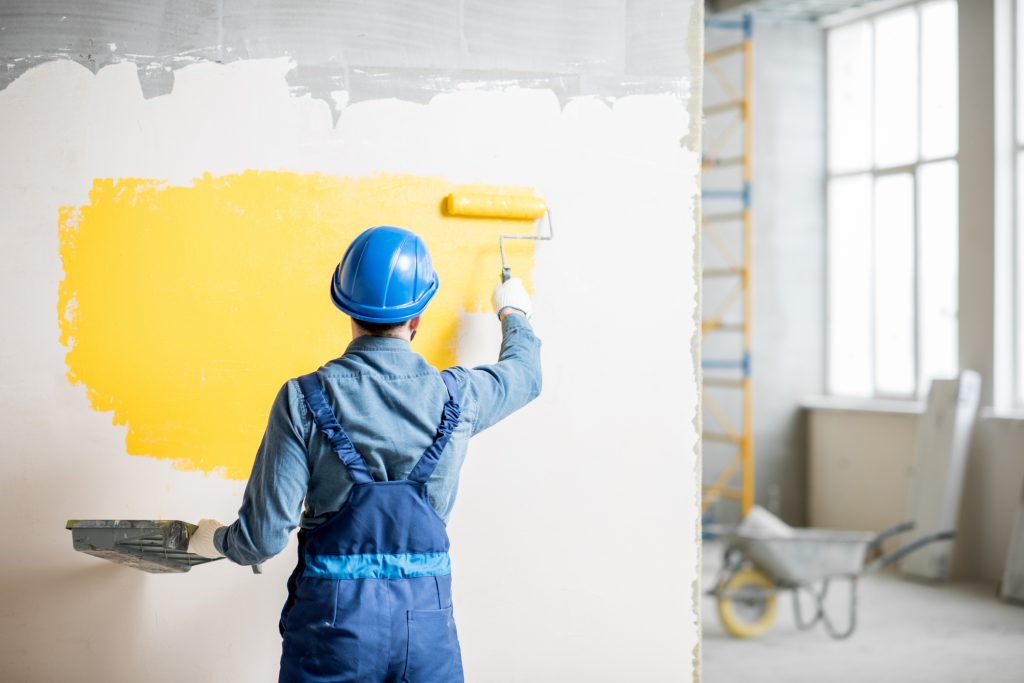 Paying Too Much Tax? Wilson Accounting Can Help. Image shows workman in uniform painting wall with yellow paint at the construction site.